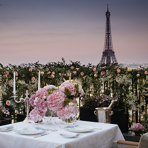 Photo of a dinner table for two in Paris at dusk with the Eiffel Tower in the background. 