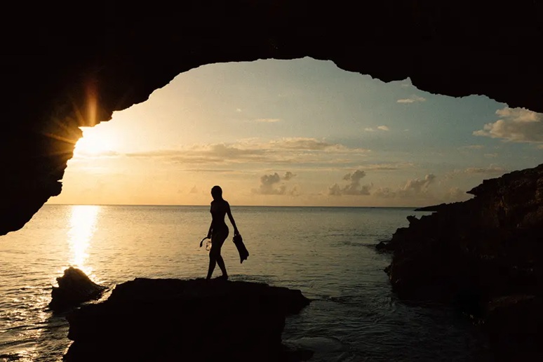 candm-Adventure-and-Nature Photo of a person silhouetted by the sunset and framed by a cave