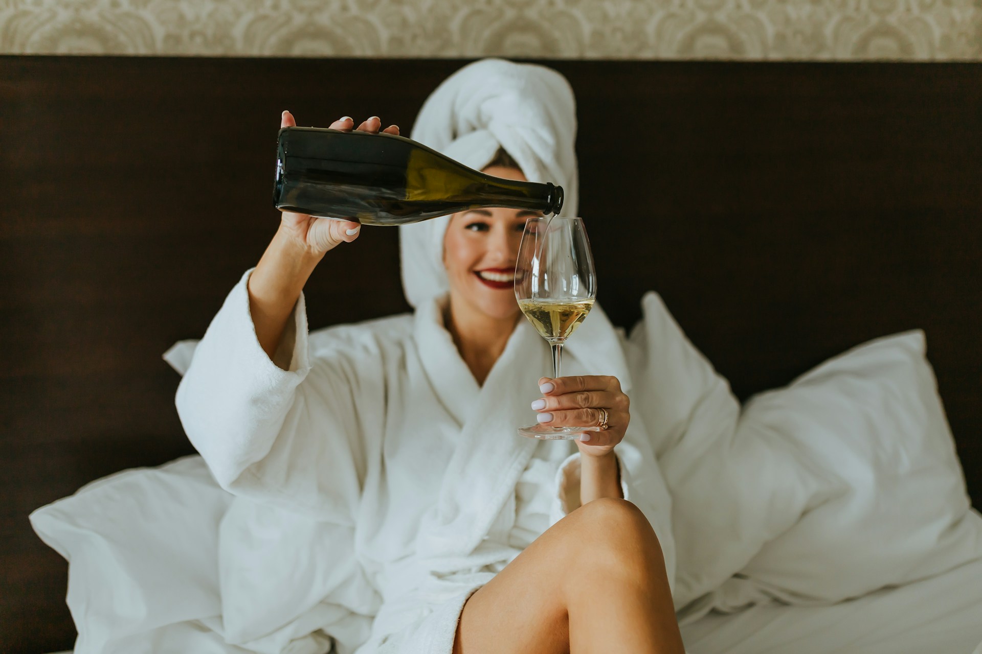 Person in a bathrobe pouring herself a glass of champagne.
