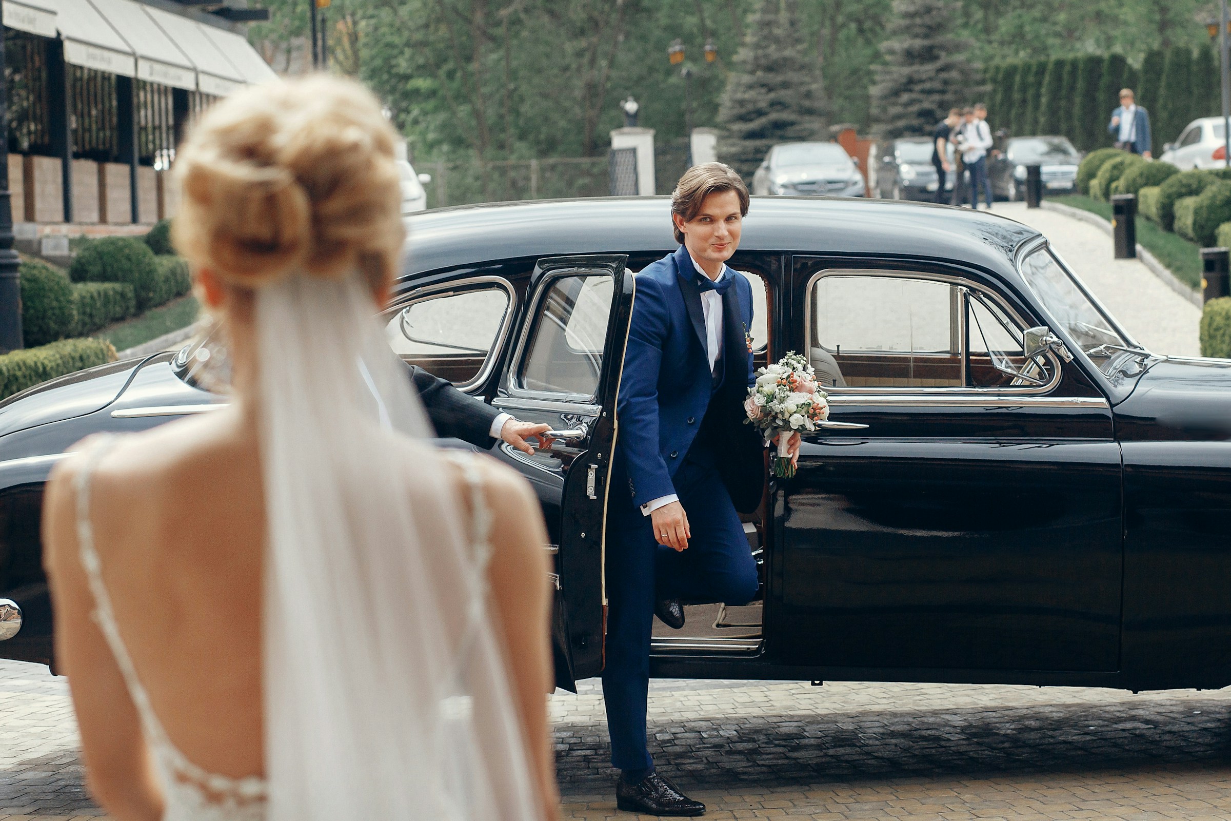 Photo of a groom waiting for his bride by a old car.